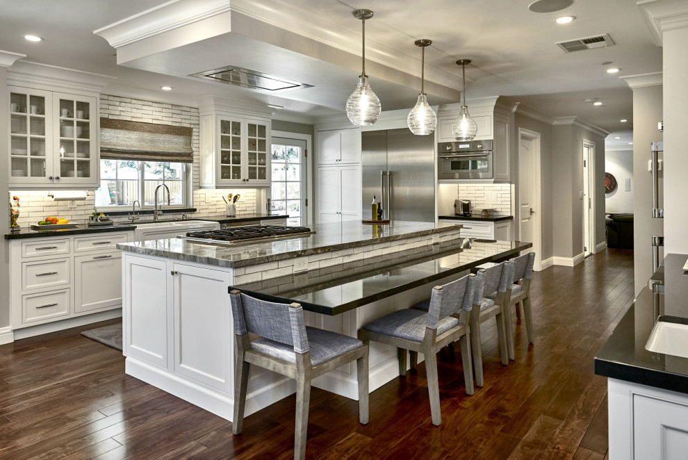 Example of a mid-sized classic u-shaped medium tone wood floor and brown floor eat-in kitchen design in San Francisco with an undermount sink, shaker cabinets, white cabinets, gray backsplash, subway tile backsplash, stainless steel appliances, an island and black countertops