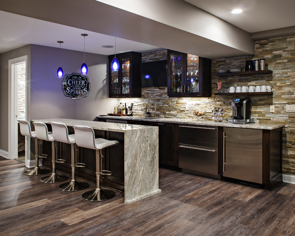 This is an example of a large transitional seated home bar in New York with an undermount sink, dark wood cabinets, stone tile splashback, dark hardwood floors and brown floor.