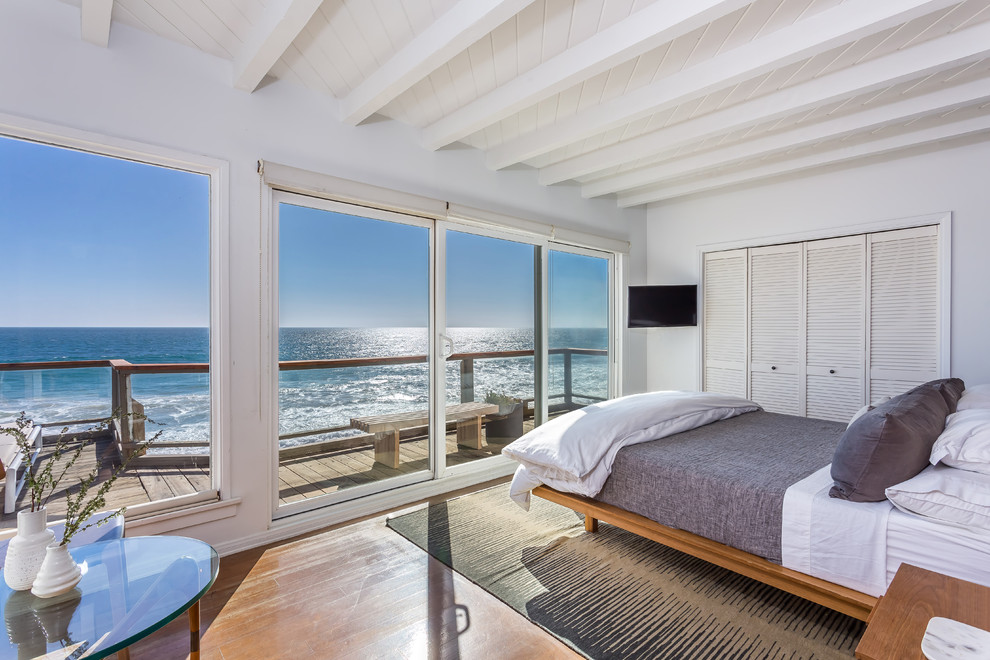 Beach style bedroom in Los Angeles with white walls, medium hardwood floors and brown floor.
