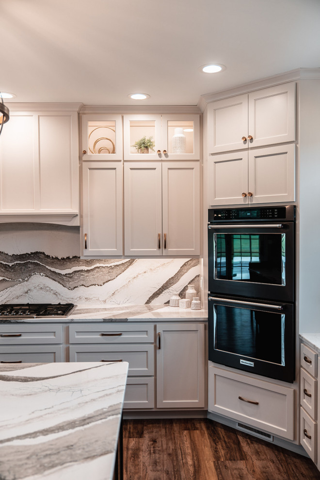 Example of a large transitional l-shaped medium tone wood floor and brown floor open concept kitchen design with an undermount sink, flat-panel cabinets, white cabinets, quartz countertops, multicolored backsplash, quartz backsplash, black appliances, an island and multicolored countertops