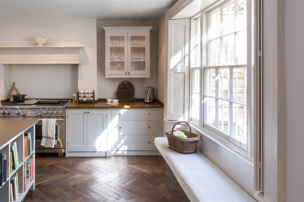 This is an example of a large transitional u-shaped eat-in kitchen in London with a double-bowl sink, shaker cabinets, white cabinets, wood benchtops, stainless steel appliances, dark hardwood floors, with island, brown floor and brown benchtop.