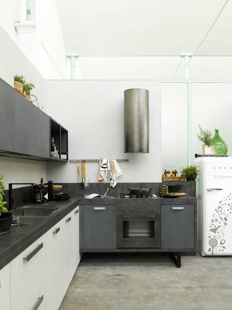 Photo of a mid-sized industrial l-shaped kitchen in Venice with a drop-in sink, black appliances, flat-panel cabinets, grey cabinets, concrete floors, grey floor, black benchtop and no island.