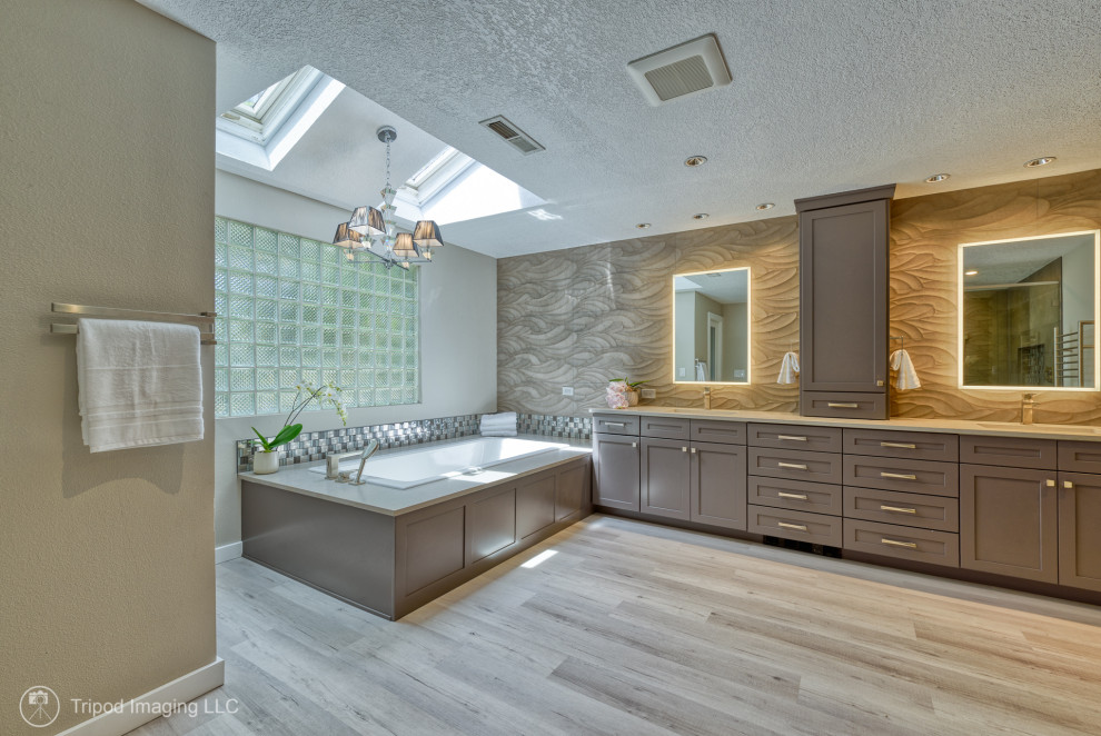 Photo of an expansive transitional master bathroom in Portland with shaker cabinets, brown cabinets, a drop-in tub, a corner shower, a two-piece toilet, gray tile, porcelain tile, grey walls, vinyl floors, an undermount sink, quartzite benchtops, grey floor, a hinged shower door, grey benchtops, a double vanity and a built-in vanity.
