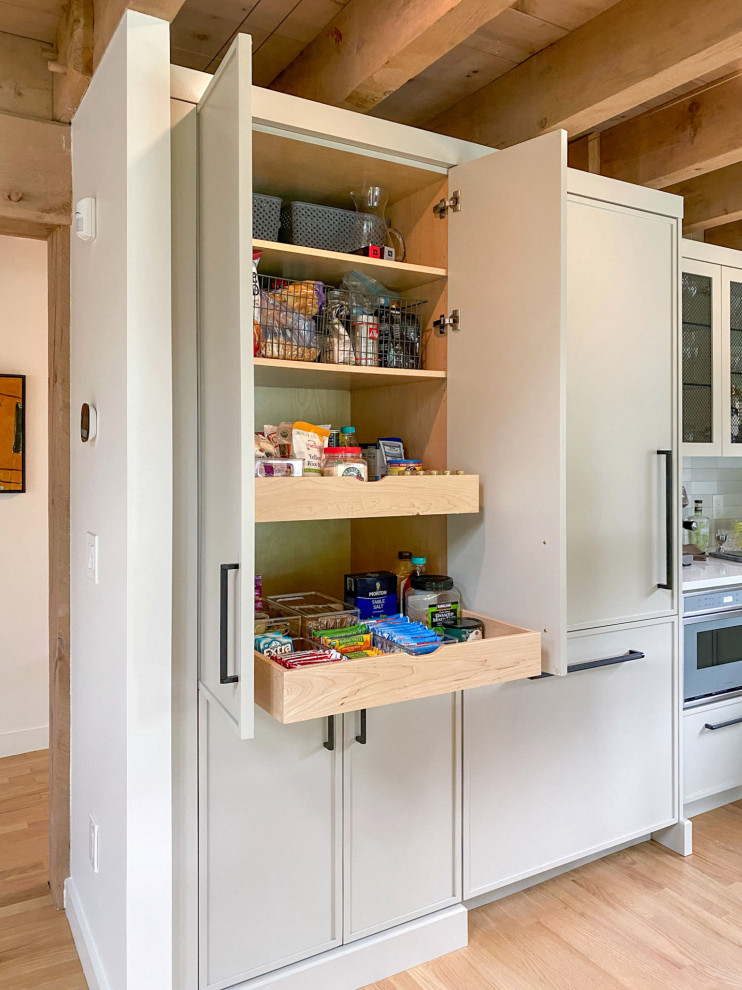 Transitional l-shaped light wood floor and exposed beam kitchen photo in Boston with a farmhouse sink, shaker cabinets, gray cabinets, quartz countertops, white backsplash, ceramic backsplash, paneled appliances, an island and white countertops