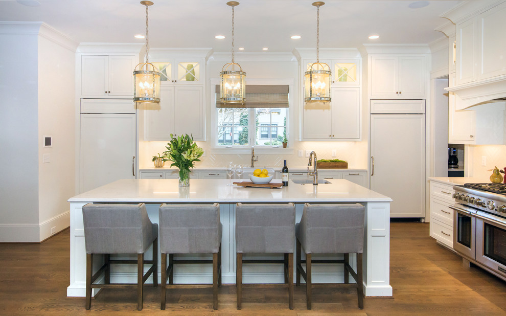 This is an example of a large transitional l-shaped eat-in kitchen in Charlotte with a farmhouse sink, flat-panel cabinets, white cabinets, quartz benchtops, white splashback, porcelain splashback, panelled appliances, dark hardwood floors, with island, brown floor and white benchtop.