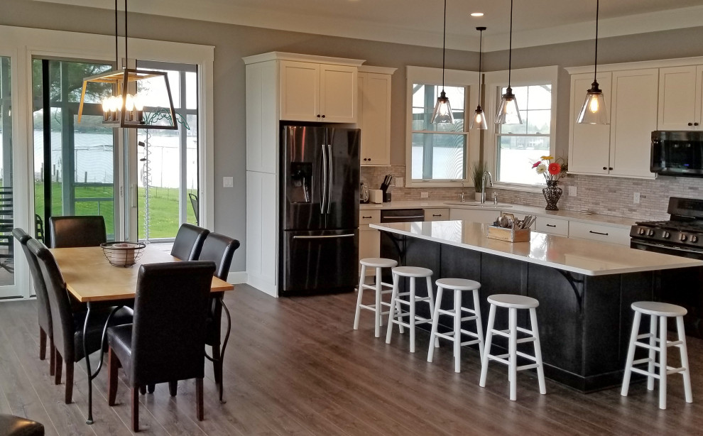 This is an example of a large transitional l-shaped kitchen in Milwaukee with a drop-in sink, flat-panel cabinets, white cabinets, quartz benchtops, beige splashback, matchstick tile splashback, black appliances, laminate floors, with island, brown floor and white benchtop.