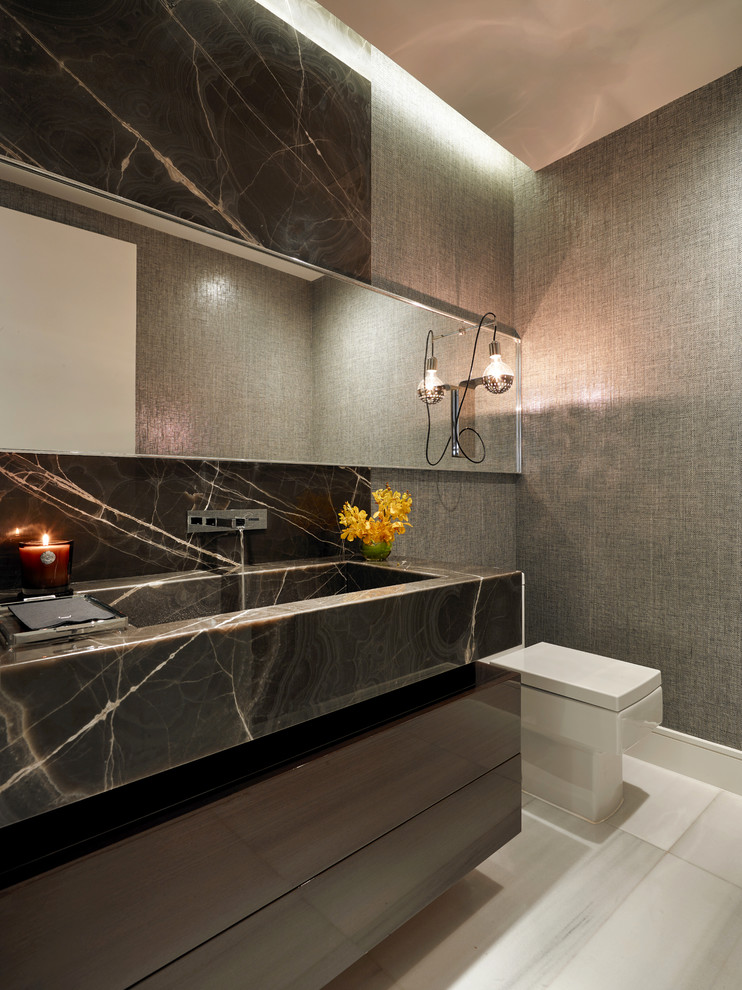 This is an example of a mid-sized contemporary powder room in Miami with a one-piece toilet, marble benchtops, flat-panel cabinets, brown cabinets, grey walls and an integrated sink.