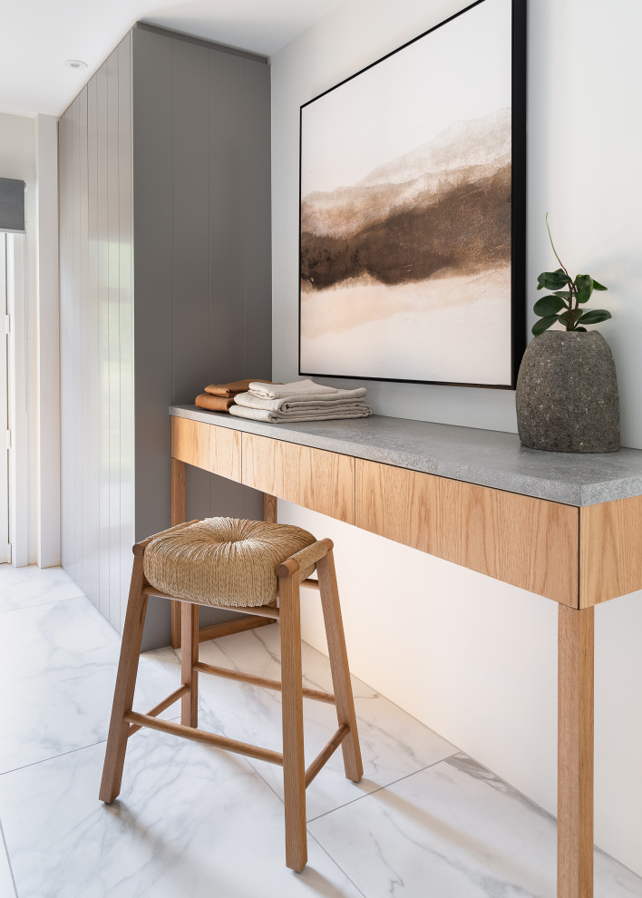 Inspiration for a mid-sized contemporary galley dedicated laundry room in Auckland with a farmhouse sink, flat-panel cabinets, light wood cabinets, quartz benchtops, grey splashback, porcelain splashback, white walls, porcelain floors, a side-by-side washer and dryer, white floor and grey benchtop.