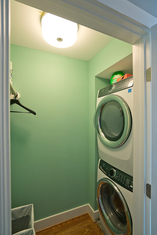 Small transitional laundry cupboard in DC Metro with green walls, medium hardwood floors, a stacked washer and dryer and brown floor.