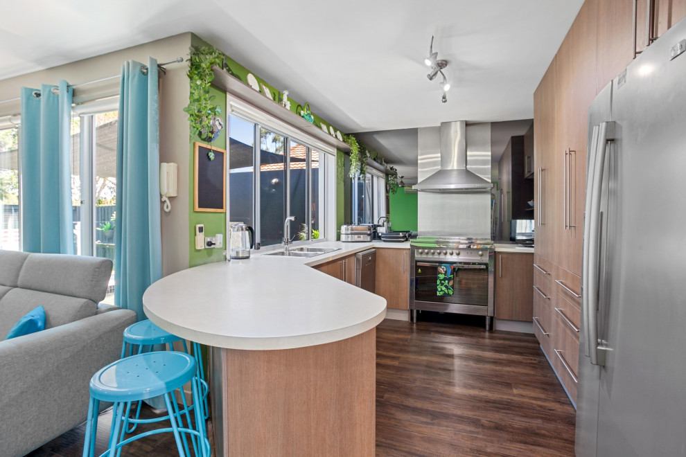 Inspiration for a tropical u-shaped kitchen in Sunshine Coast with a double-bowl sink, medium wood cabinets, laminate benchtops, green splashback, stainless steel appliances, vinyl floors, brown floor and white benchtop.