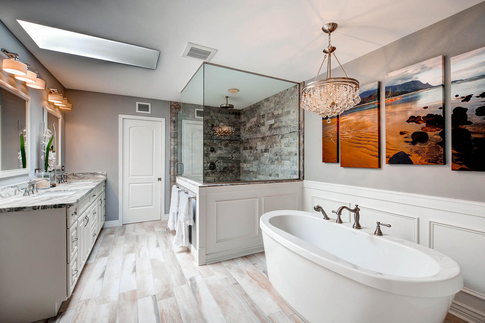 Large transitional master bathroom in Phoenix with raised-panel cabinets, white cabinets, a freestanding tub, gray tile, porcelain tile, grey walls, porcelain floors, an undermount sink, granite benchtops, a corner shower and a hinged shower door.