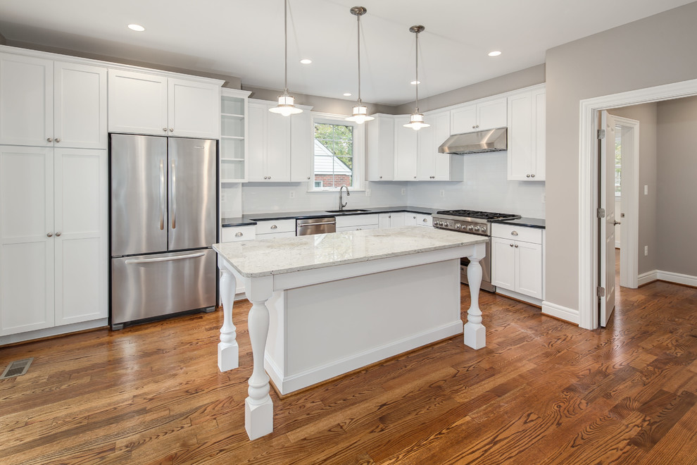 This is an example of a large transitional l-shaped open plan kitchen in DC Metro with an undermount sink, shaker cabinets, white cabinets, white splashback, stainless steel appliances, medium hardwood floors, with island and subway tile splashback.