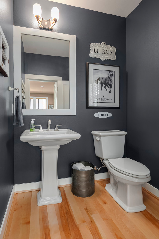 Photo of a mid-sized transitional powder room in Seattle with a two-piece toilet, grey walls, light hardwood floors, a pedestal sink, solid surface benchtops and brown floor.