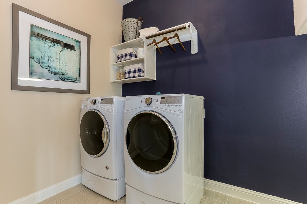 Photo of a mid-sized country single-wall dedicated laundry room in Other with open cabinets, blue walls, ceramic floors, a side-by-side washer and dryer, beige floor and white cabinets.