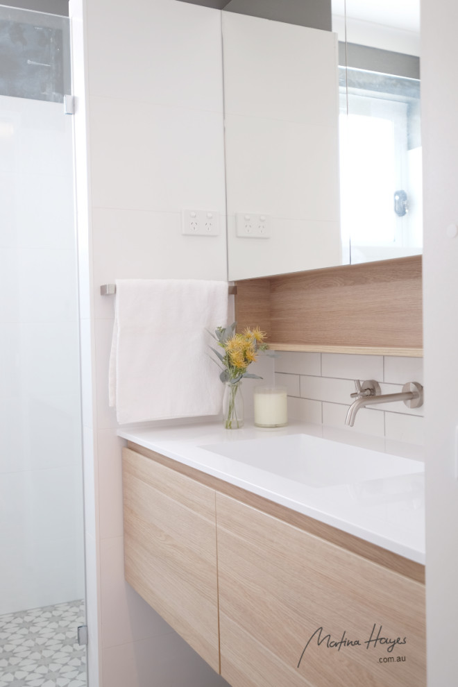 This is an example of a mid-sized contemporary master bathroom in Sydney with flat-panel cabinets, light wood cabinets, white tile, ceramic tile, a drop-in sink, engineered quartz benchtops, grey floor, white benchtops, a laundry, a single vanity, a built-in vanity, a curbless shower, a one-piece toilet, white walls, porcelain floors and an open shower.
