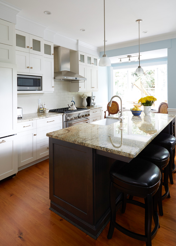 Inspiration for a transitional medium tone wood floor eat-in kitchen remodel in DC Metro with a farmhouse sink, recessed-panel cabinets, white cabinets, granite countertops, white backsplash, subway tile backsplash, stainless steel appliances and an island