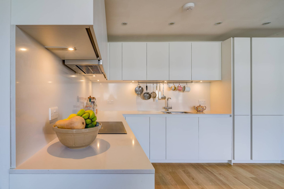 Example of a mid-sized trendy l-shaped light wood floor and brown floor eat-in kitchen design in London with a double-bowl sink, flat-panel cabinets, white cabinets, quartzite countertops, white backsplash, black appliances, no island and white countertops