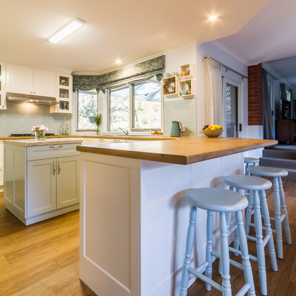 This is an example of a mid-sized traditional u-shaped eat-in kitchen in Melbourne with a drop-in sink, shaker cabinets, white cabinets, wood benchtops, blue splashback, porcelain splashback, stainless steel appliances, medium hardwood floors, a peninsula, brown floor and brown benchtop.