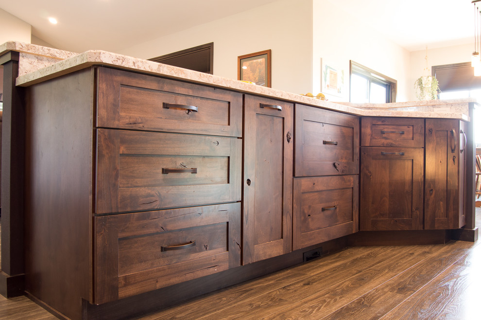 Mountain style l-shaped brown floor eat-in kitchen photo with shaker cabinets, brown cabinets, laminate countertops, gray backsplash, stainless steel appliances, an island and beige countertops