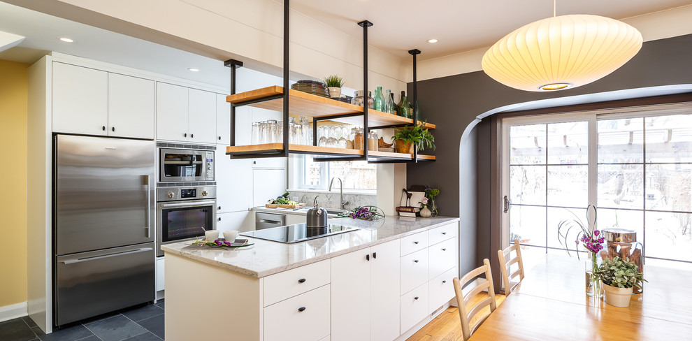 Photo of a small industrial u-shaped eat-in kitchen in Ottawa with flat-panel cabinets, white cabinets, granite benchtops, white splashback, stainless steel appliances, with island, an undermount sink, stone slab splashback, slate floors and grey floor.