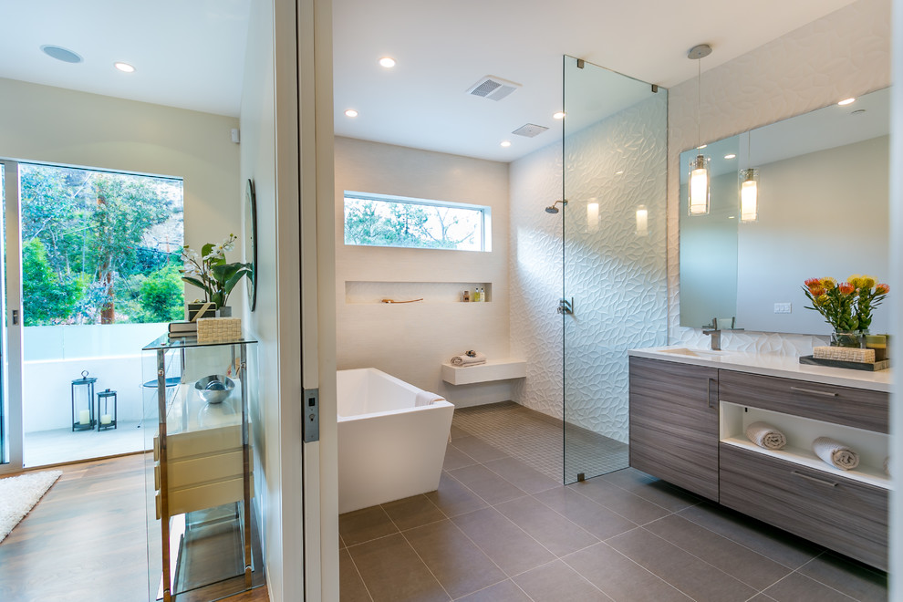 Photo of a modern master bathroom in Los Angeles with a drop-in sink, flat-panel cabinets, grey cabinets, engineered quartz benchtops, a freestanding tub, an open shower, a one-piece toilet, brown tile, porcelain tile, white walls and medium hardwood floors.