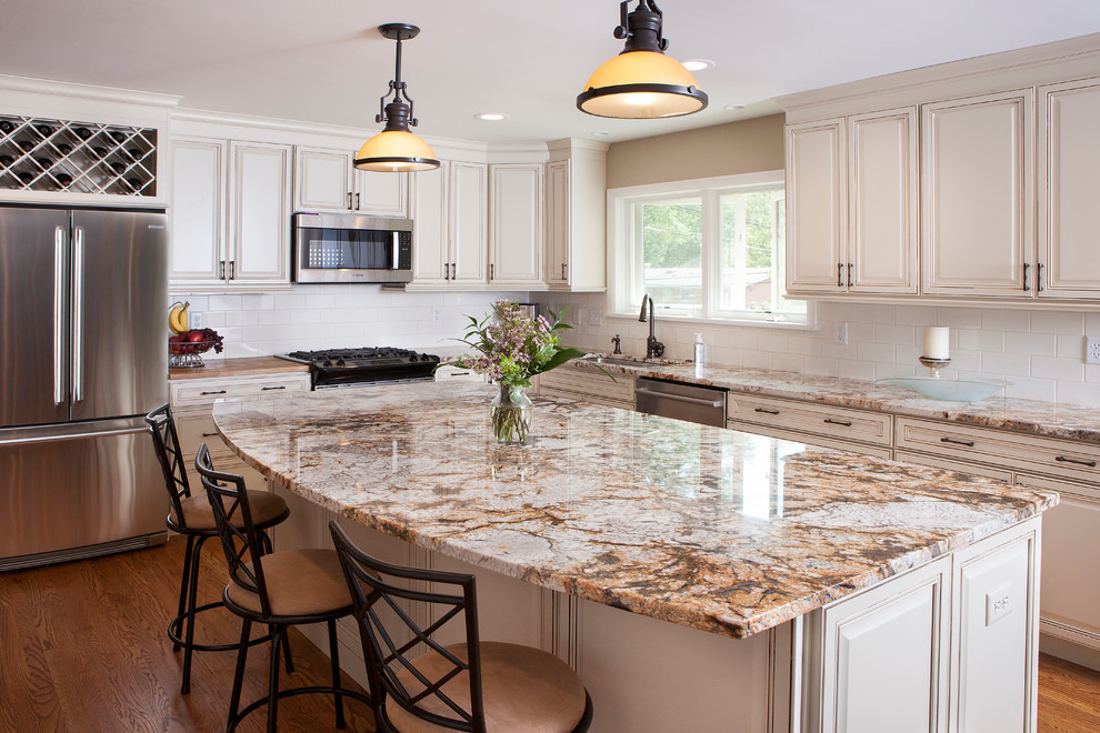 Large transitional l-shaped open plan kitchen in St Louis with an undermount sink, raised-panel cabinets, white cabinets, granite benchtops, white splashback, subway tile splashback, stainless steel appliances, medium hardwood floors, with island, brown floor and brown benchtop.