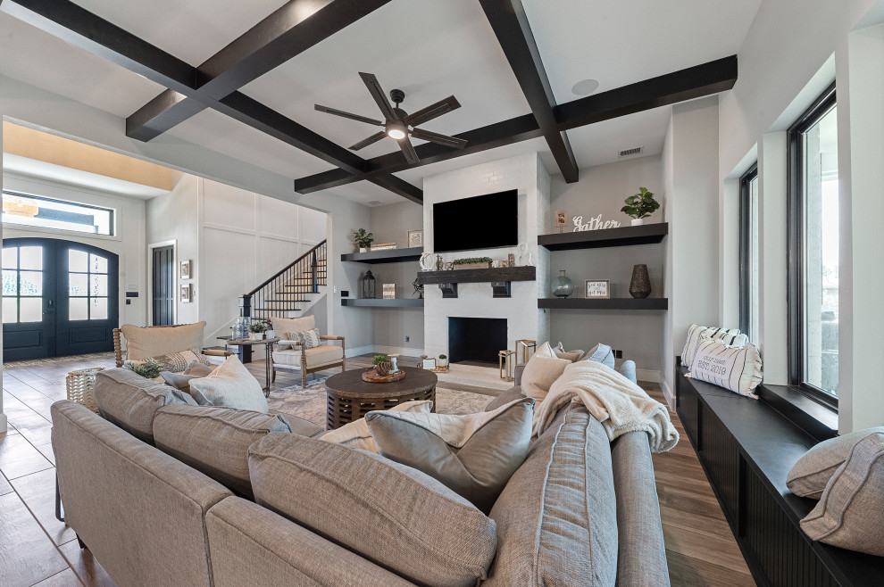 Design ideas for a large country open concept family room in Dallas with grey walls, medium hardwood floors, a wood stove, a brick fireplace surround, a wall-mounted tv, brown floor and exposed beam.