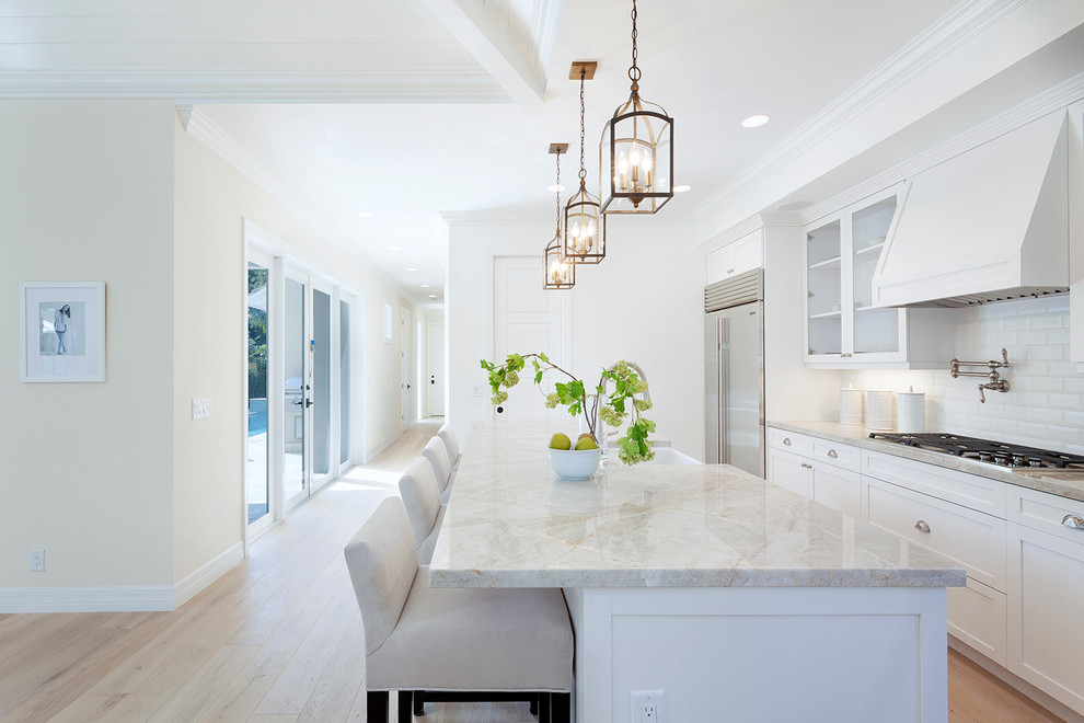 Inspiration for a traditional kitchen in Miami with a farmhouse sink, shaker cabinets, white cabinets, white splashback, subway tile splashback, stainless steel appliances, light hardwood floors and with island.