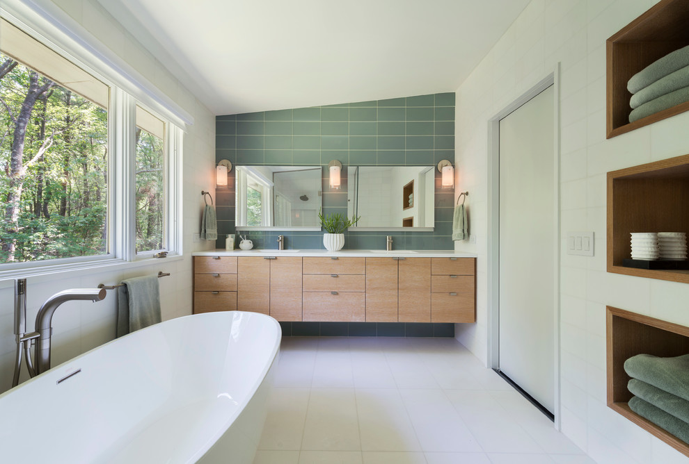 Photo of a large midcentury bathroom in Boston with a freestanding tub, an undermount sink, flat-panel cabinets, light wood cabinets, marble benchtops, green tile, glass tile, white walls and white benchtops.