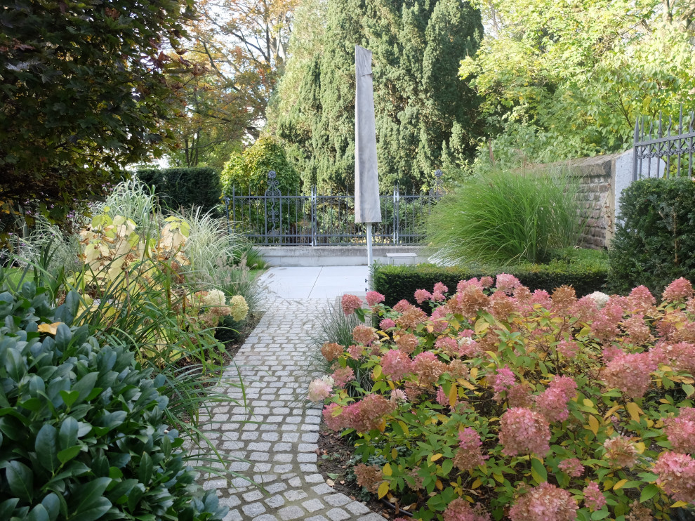 Cette photo montre un jardin à la française latéral tendance de taille moyenne et l'automne avec un massif de fleurs, une exposition partiellement ombragée, des pavés en béton et une clôture en métal.
