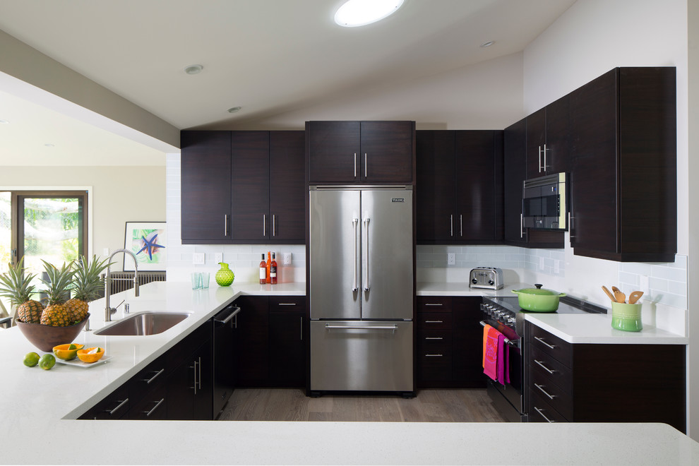 Photo of a large tropical u-shaped open plan kitchen in Hawaii with a single-bowl sink, flat-panel cabinets, dark wood cabinets, white splashback, glass tile splashback, stainless steel appliances and a peninsula.