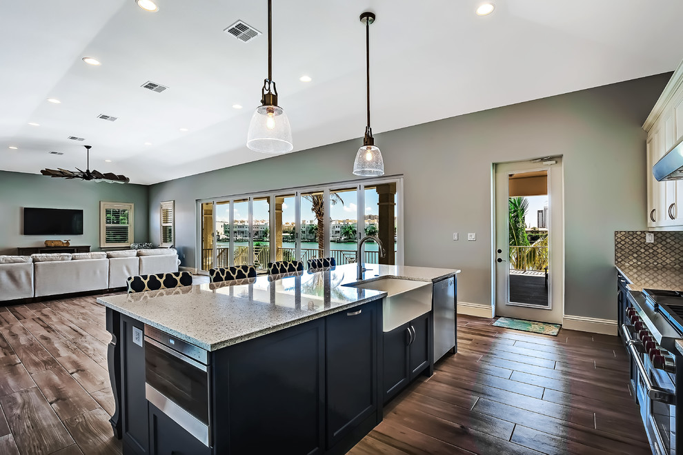 This is an example of a large transitional l-shaped open plan kitchen in Tampa with a farmhouse sink, shaker cabinets, white cabinets, recycled glass benchtops, multi-coloured splashback, porcelain splashback, stainless steel appliances, porcelain floors and with island.