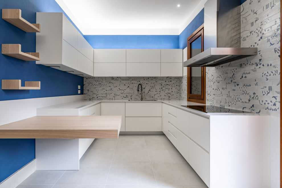 This is an example of a mid-sized contemporary u-shaped open plan kitchen in Venice with a double-bowl sink, beaded inset cabinets, light wood cabinets, quartzite benchtops, blue splashback, ceramic splashback, stainless steel appliances, ceramic floors, with island, white floor and white benchtop.
