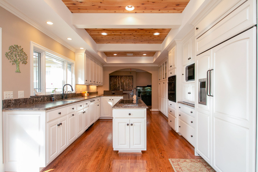 Example of a large minimalist galley light wood floor and brown floor eat-in kitchen design with a single-bowl sink, raised-panel cabinets, white cabinets, quartzite countertops, brown backsplash, paneled appliances, an island and brown countertops