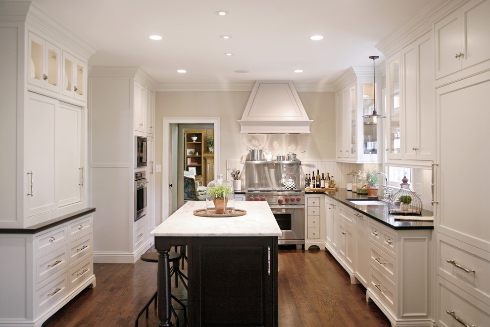 Inspiration for a large traditional u-shaped kitchen in Atlanta with an undermount sink, recessed-panel cabinets, white cabinets, panelled appliances, white splashback, solid surface benchtops, medium hardwood floors, with island and brown floor.