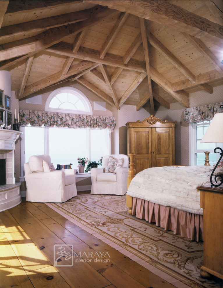 This is an example of a large beach style master bedroom in Santa Barbara with light hardwood floors, a standard fireplace, a stone fireplace surround and brown walls.
