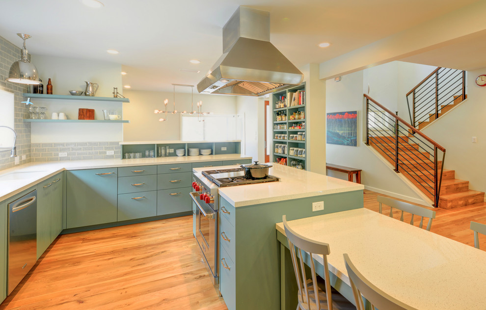 This is an example of a mid-sized midcentury l-shaped eat-in kitchen in Austin with an undermount sink, flat-panel cabinets, green cabinets, quartz benchtops, grey splashback, ceramic splashback, stainless steel appliances, medium hardwood floors and with island.