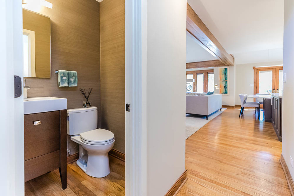 This is an example of a small arts and crafts powder room in Chicago with flat-panel cabinets, brown cabinets, a two-piece toilet, grey walls, medium hardwood floors, an integrated sink, solid surface benchtops, brown floor and white benchtops.