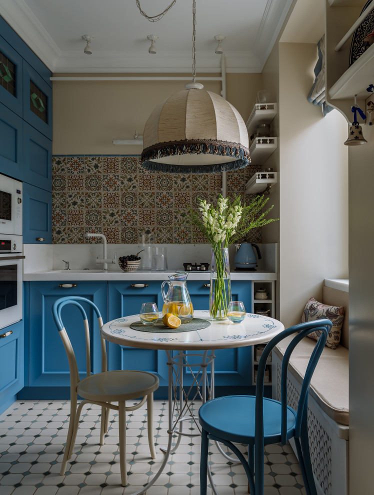 Foto på ett lantligt vit kök, med blå skåp, flerfärgad stänkskydd och flerfärgat golv
