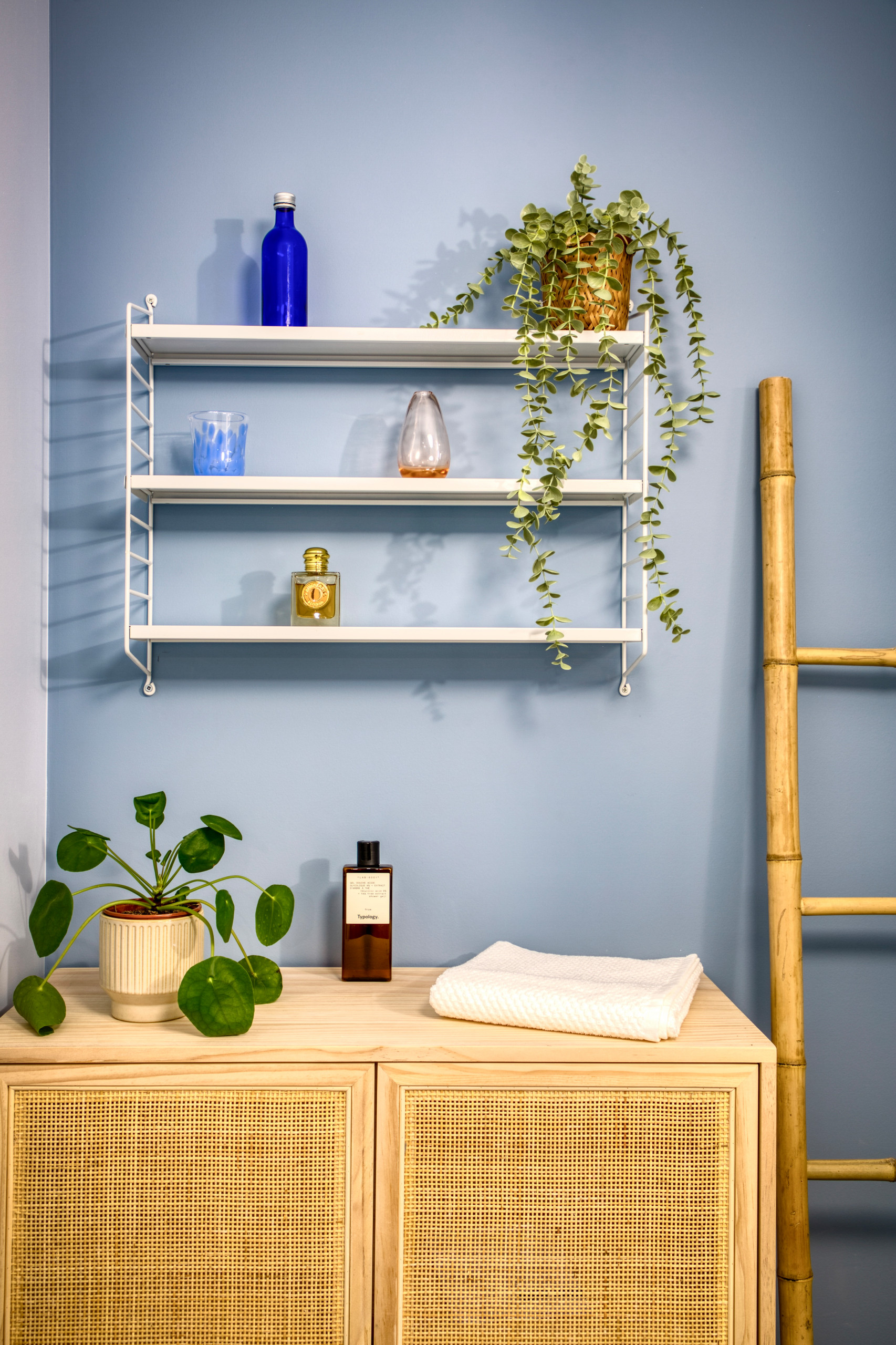 Cette salle de bain toute blanche s'est parée de 2 nuances de bleu, au mur et de meubles naturels surmontée d'une étagère blanche.