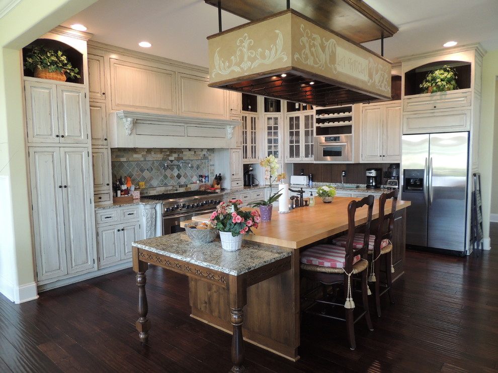 Large traditional l-shaped eat-in kitchen in Indianapolis with a farmhouse sink, raised-panel cabinets, distressed cabinets, granite benchtops, multi-coloured splashback, ceramic splashback, stainless steel appliances, dark hardwood floors and with island.