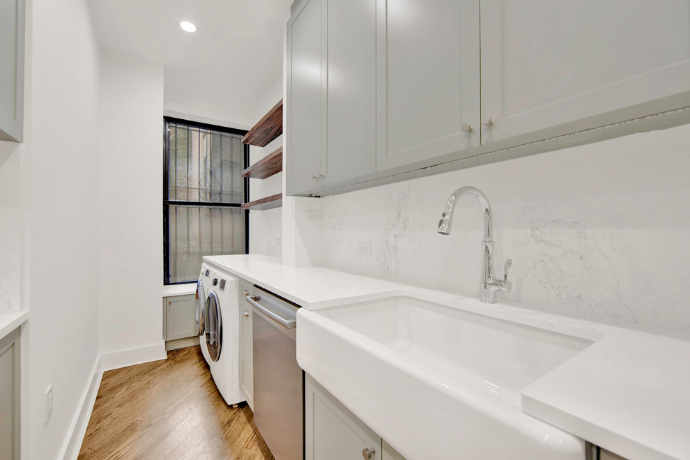 Photo of a small classic galley utility room in New York with a built-in sink, flat-panel cabinets, green cabinets, engineered stone countertops, white splashback, ceramic splashback, white walls, medium hardwood flooring, a side by side washer and dryer, brown floors and white worktops.