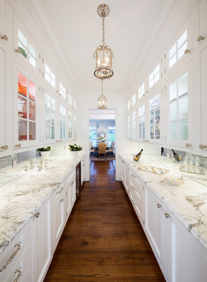 This is an example of a mid-sized beach style galley home bar in DC Metro with glass-front cabinets, white cabinets, marble benchtops and medium hardwood floors.