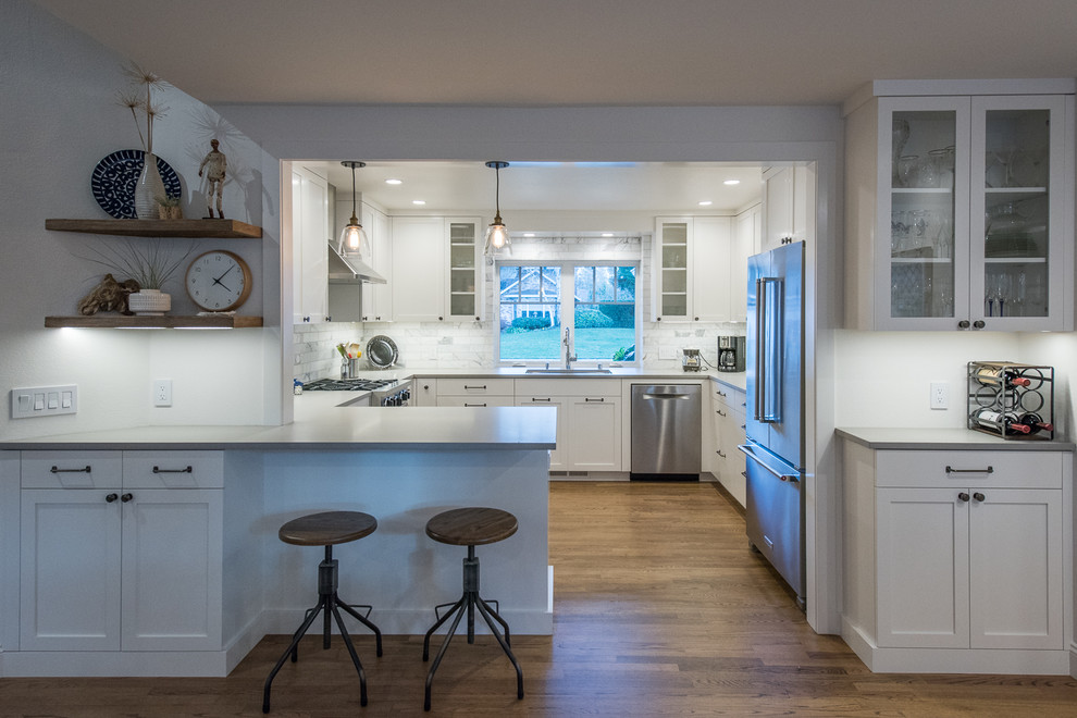 Transitional medium tone wood floor kitchen photo with white cabinets, gray backsplash and stainless steel appliances