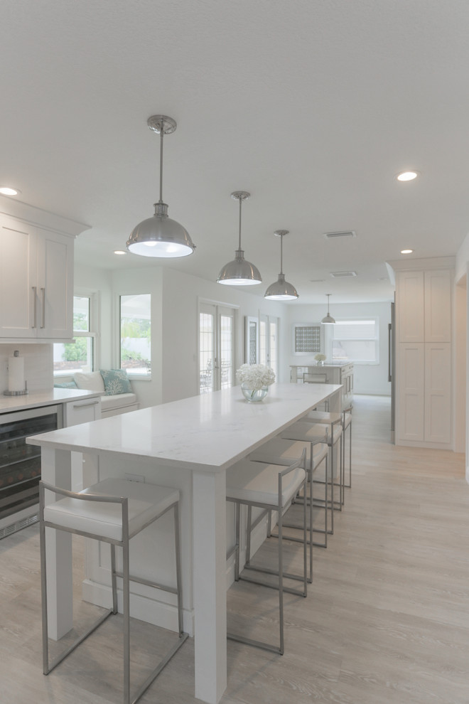 Inspiration for an expansive modern galley open plan kitchen in Tampa with a farmhouse sink, shaker cabinets, white cabinets, quartz benchtops, white splashback, marble splashback, stainless steel appliances, vinyl floors, multiple islands and grey floor.