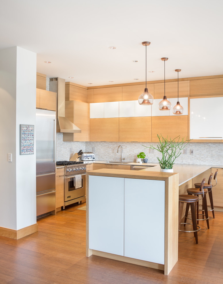 Design ideas for a contemporary kitchen in Portland with flat-panel cabinets, light wood cabinets, stainless steel appliances, light hardwood floors, with island and solid surface benchtops.