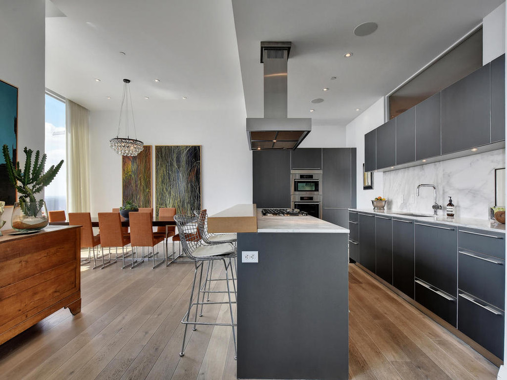 Photo of a contemporary l-shaped open plan kitchen in Austin with a single-bowl sink, flat-panel cabinets, grey cabinets, marble benchtops, white splashback, stone slab splashback, stainless steel appliances, with island and medium hardwood floors.