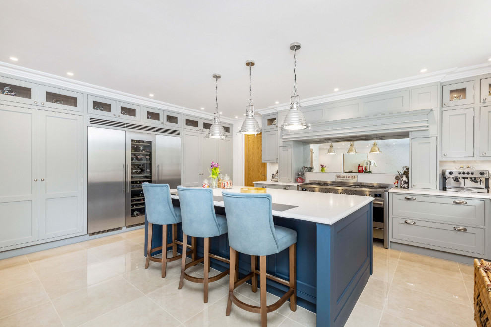 Inspiration for a traditional u-shaped open plan kitchen in Surrey with an undermount sink, shaker cabinets, blue cabinets, marble benchtops, mirror splashback, stainless steel appliances, limestone floors, with island, beige floor and grey benchtop.