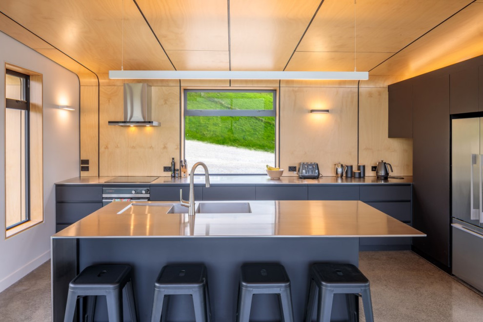 Photo of a mid-sized contemporary l-shaped eat-in kitchen in Christchurch with a double-bowl sink, flat-panel cabinets, black cabinets, stainless steel benchtops, multi-coloured splashback, timber splashback, stainless steel appliances, concrete floors, with island, grey floor and grey benchtop.