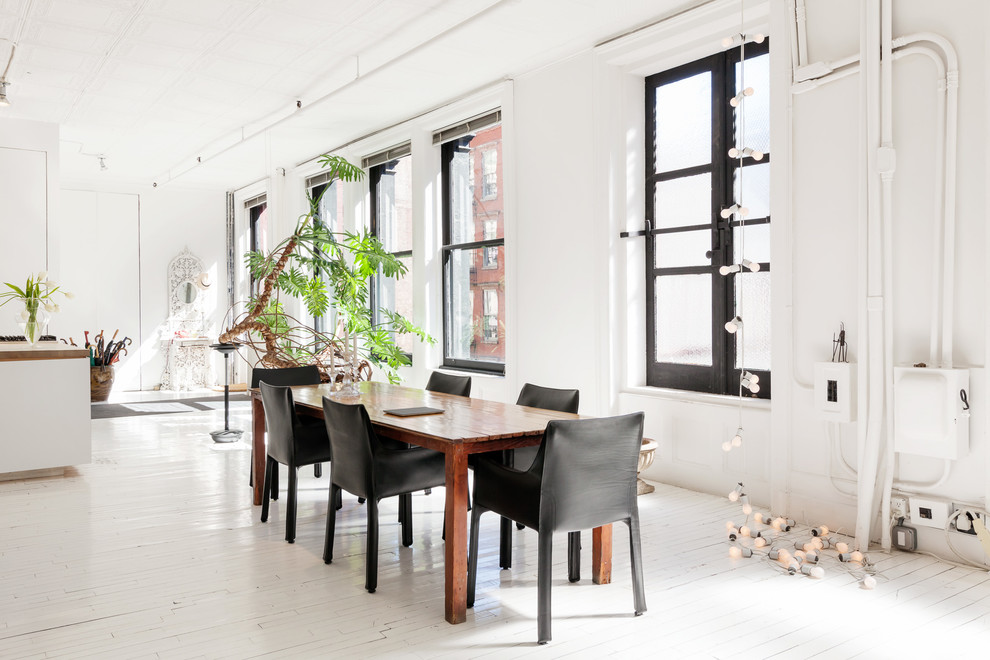 This is an example of an industrial dining room in New York with white walls and painted wood floors.